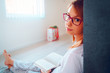 © Miljan Živković - Portrait of young beautiful woman girl student reading or study at home lying on the floor in by the bed wearing glasses holding a book looking to the camera