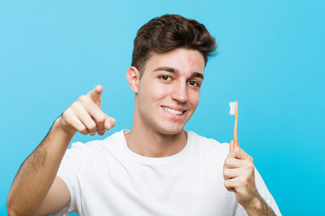 Wall Mural - Young caucasian man holding a toothbrush Young indian woman wearing a pajamas and sleep mask isolated holding a pillow cheerful smiles pointing to front.< mixto >