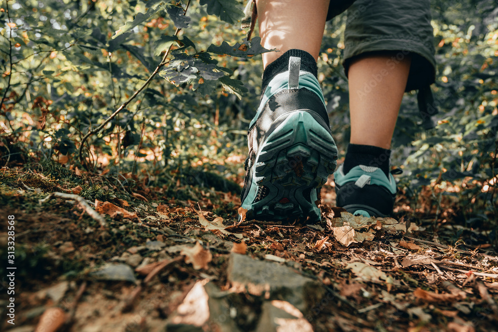 Muddy boots of hiker on forest trail. Traveler feet are stepping on the ground with fallen leaves. Close up of the sole of dirty shoes. Adventure and hiking concept outdoor. Hipster lifestyle - obrazy, fototapety, plakaty 