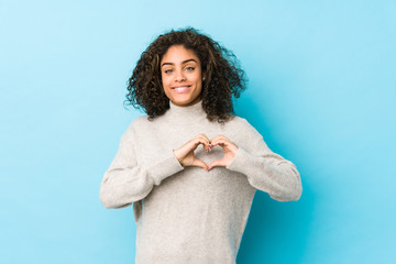 Wall Mural - Young african american curly hair woman smiling and showing a heart shape with hands.