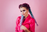 Beautiful stylish girl with colorful kanekalon braided in her hair. Pretty woman with colorful violet ombre hair and pro makeup isolated at pink background. Hairdresser salon concept.