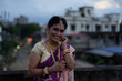 © abir - Portrait of a beautiful smiling brunette Indian Bengali bride in traditional sari standing on the roof top in afternoon under blue sky. Indian lifestyle.