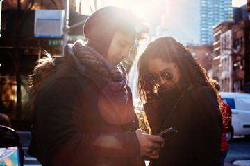 Portrait of a young hispanic couple looking at phone outside on a sunny urban street