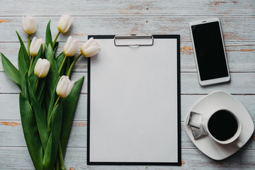 Wall Mural - White Tulip bouquet on wooden blue background with coffee Cup, smartphone and blank paper tablet