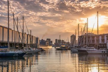 Wall Mural - Genova, Genoa, Liguria, Italy: Beautiful sunset view of old harbor (Porto Antico), sailboats docked at quay nearby aquarium, reflections on water, sun setting