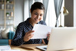 © fizkes - Smiling indian woman holding reading paper letter sit at table