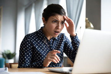 Shocked young indian girl look at laptop screen feel terrified