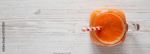 Fotomural Homemade Mango Carrot Smoothie in a glass jar mug over white wooden background, top view