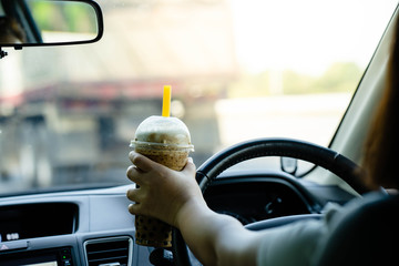 Human hand holding ice coffee while driving.