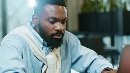 Portrait of african american handsome male using laptop for work in modern office programmer serious looks at monitor screen freelance successful worker businessman. Slow motion, close up.