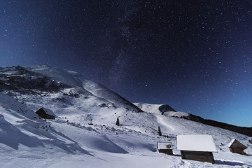 Wall Mural - Fairytale landscapes of the winter Carpathian Mountains with a charming milky way in the sky tourist tents and snowy houses in the valleys	