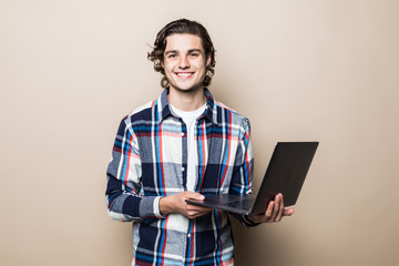 portrait of attractive cheerful man holding in hands laptop isolated over beige color background