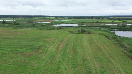 Wall Mural - Aerial video. Rolling haystacks in countryside on the field on a cloudy day. A loader tractor loads harvested straw in bales on a tractor with a trailer for transportation