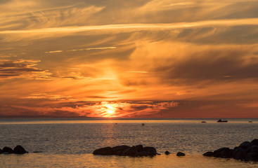 Wall Mural - Evening sunlight on coast, yellow clouds, golden sky reflection on water. Beach in summer. Seaside natural environment. Shore in Harilaid, small island in Estonia. Nature Reserve in North Europe