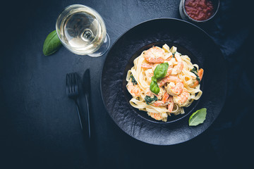 Wall Mural - Italian pasta fettuccine in a creamy sauce with shrimp on a black plate, top view