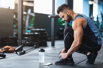 young athlete tying sneakers laces at gym