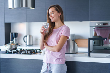 Happy attractive joyful smiling brunette woman drinking fresh clean filtered purified water at kitchen at home. Healthy lifestyle and quench thirst