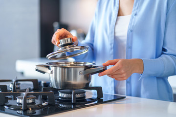 Woman housewife using steel metallic saucepan for preparing dinner in the kitchen at home. Kitchenware for cooking