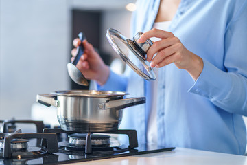 Female housewife using steel metallic saucepan for preparing dinner in the kitchen at home. Kitchenware for cooking