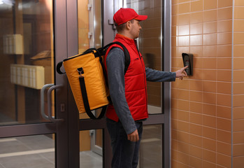 Canvas Print - Male courier with thermo bag pushing intercom button. Food delivery service