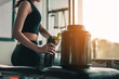 © Take Production - fitness ,workout, gym exercise ,lifestyle  and healthy concept. A side view of a woman sitting to relax after a workout, holding protein shake bottle and whey protein placed beside at the sunset.
