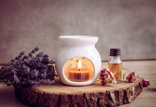 Vintage Style Picture Of White Ceramic Candle Aroma Oil Lamp With Essential Oil Bottle And Dry Flower Petals On Natural Pine Wood Disc, Dry Background With Copy Space.