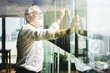 © Shutter B - Retirement concept. Senior grey-haired businessman standing and looking to right hand at modern business lounge high up in an office tower.
