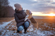 young woman on a walk with a Beagle dog on a winter evening against a beautiful sunset