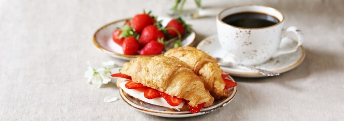 Wall Mural - Breakfast in French. Croissant sandwich with I soft cheese and strawberries. And black coffee, a bouquet of flowers. Fresh strawberries. Soft focus. Space for text.  Copy Space