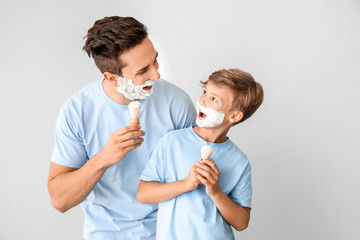 Wall Mural - Funny father and his little son shaving against grey background