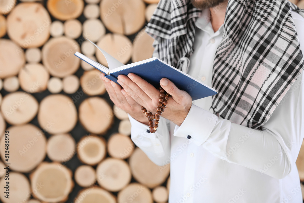 Muslim man with Koran and beads on wooden background