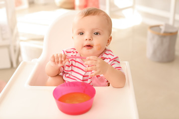 Wall Mural - Portrait of cute little baby eating tasty food in kitchen