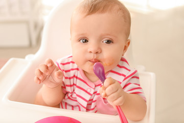 Portrait of cute little baby eating tasty food in kitchen