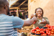 © Confidence - black girl selling tomatoes in a local african market to a male customer smiling and feeling happy and satisfied
