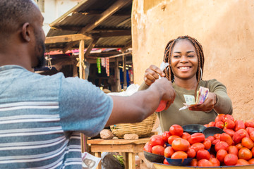 black girl selling tomatoes in a local african market to a male customer smiling and feeling happy a