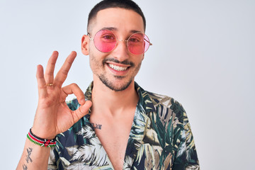 Wall Mural - Young handsome man wearing Hawaiian sumer shirt and pink sunglasses over isolated background doing ok sign with fingers, excellent symbol