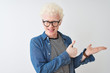 © Krakenimages.com - Young albino blond man wearing denim shirt and glasses over isolated white background Showing palm hand and doing ok gesture with thumbs up, smiling happy and cheerful