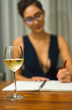 © Wes - A woman wearing glasses sits at a table drinking white wine and writing in a journal