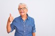 © Krakenimages.com - Senior grey-haired woman wearing denim shirt and glasses over isolated white background doing happy thumbs up gesture with hand. Approving expression looking at the camera showing success.