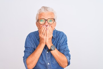 Wall Mural - Senior grey-haired woman wearing denim shirt and glasses over isolated white background laughing and embarrassed giggle covering mouth with hands, gossip and scandal concept