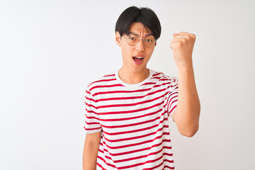 Wall Mural - Young chinese man wearing glasses and striped t-shirt standing over isolated white background angry and mad raising fist frustrated and furious while shouting with anger. Rage and aggressive concept.