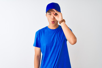 Wall Mural - Chinese deliveryman wearing blue t-shirt and cap standing over isolated white background doing ok gesture shocked with surprised face, eye looking through fingers. Unbelieving expression.