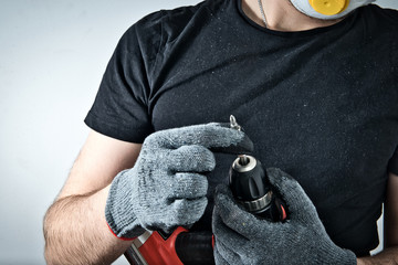Poster - The worker uses a screwdriver. Fastening the screw to the screwdriver. The man holds a red screwdriver in his hand, doing renovation at home, refreshing the apartment, home.
