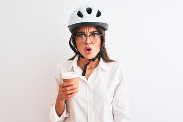 Wall Mural - Beautiful businesswoman wearing bike helmet drinking coffee over isolated white background scared in shock with a surprise face, afraid and excited with fear expression