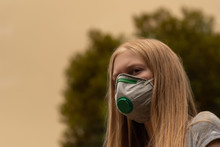 Australian Bushfire: Blond Girl Wearing P2 N95 Protection Respiratory Mask To Reduce Amount Of Breathing PM2.5 Particles From Bushfire Smoke.