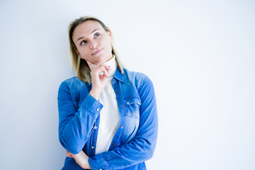 Young beautiful woman wearing denim shirt standing over isolated white background with hand on chin thinking about question, pensive expression. Smiling with thoughtful face. Doubt concept.