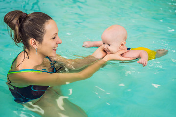 Beautiful mother teaching cute baby girl how to swim in a swimming pool. Child having fun in water with mom