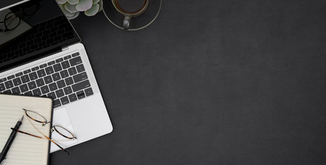 Top view of dark stylish workplace with laptop, coffee cup and office supplies on black desk