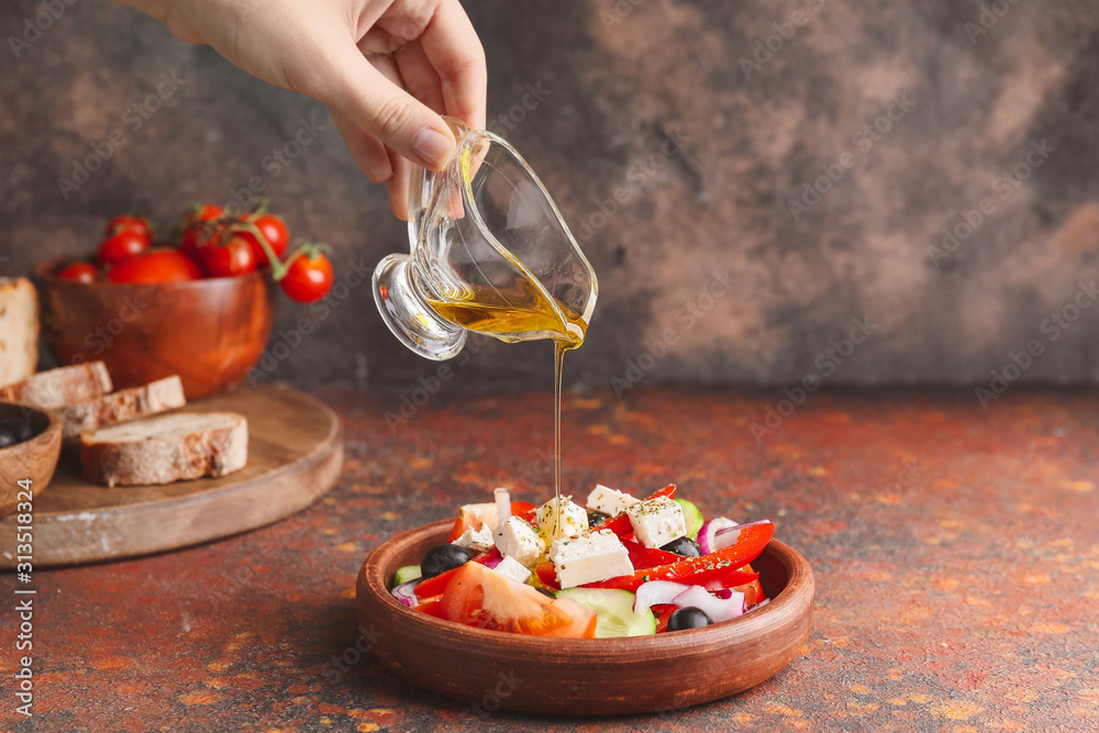 Woman dressing fresh Greek salad on table
