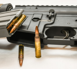 An multi colored AR 15 rifle with a rifle magazine loaded with 223 caliber bullets on it with two of the same bullets in front of it on a white background